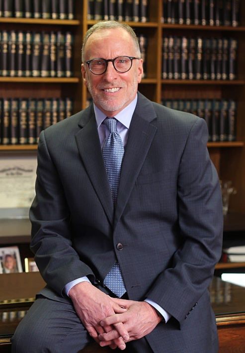 A man in a suit and tie is sitting in front of a bookshelf.